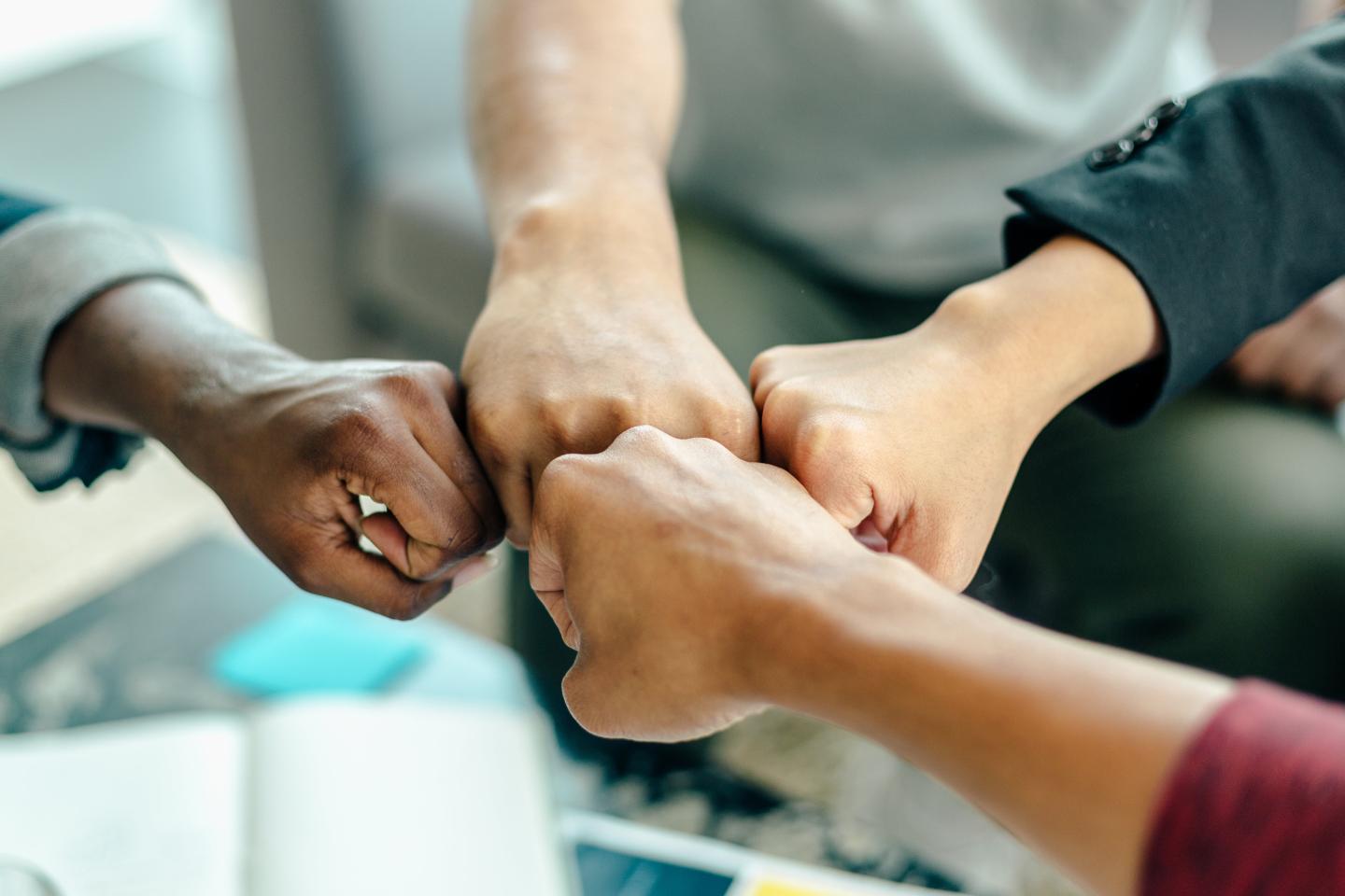 Five hands in a fist bump, showing unity and teamwork.