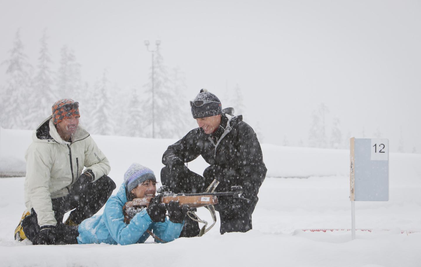 person laying down shooting on the biathlon range with coaches beside them